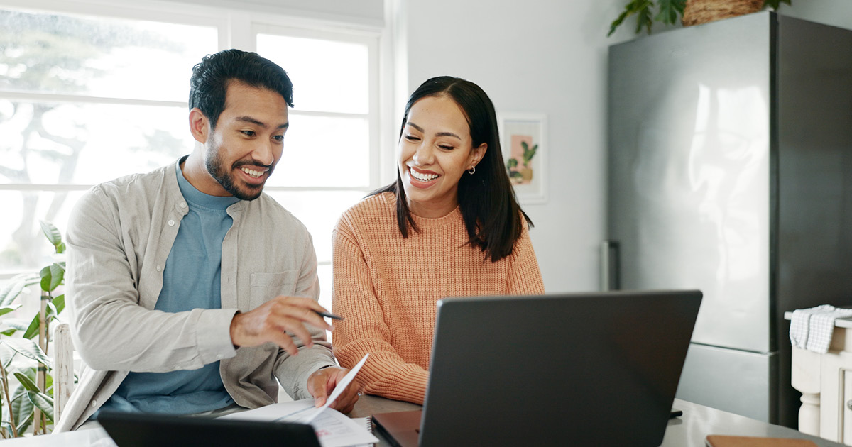 smiling man and woman pointing at a computer screen.
